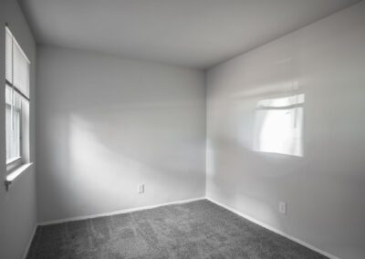 A spacious empty room featuring a gray carpet and pristine white walls, creating a minimalist and serene atmosphere